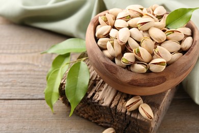 Delicious pistachios in bowl on wooden table, closeup