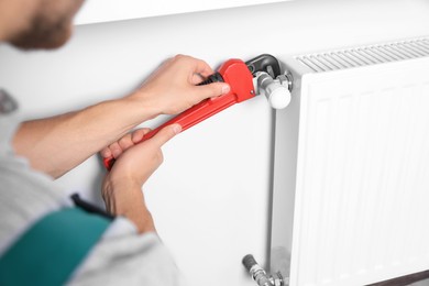 Photo of Professional plumber using adjustable wrench for installing new heating radiator indoors, closeup