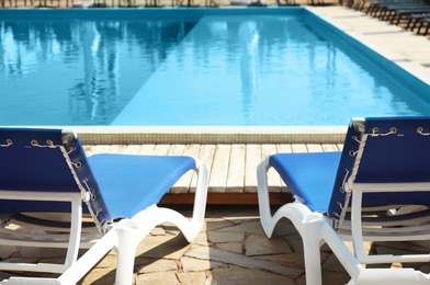 Comfortable loungers at clean swimming pool on sunny day