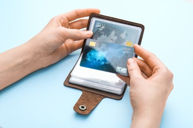 Photo of Woman holding leather card holder with credit cards on light blue background, closeup