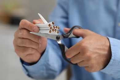 Photo of Stop smoking concept. Man cutting cigarettes on blurred background, closeup
