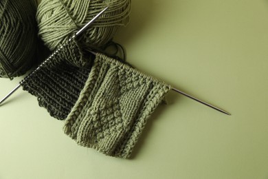 Photo of Knitting, needles and soft yarns on light green background, above view. Space for text