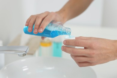 Photo of Young man using mouthwash in bathroom, closeup