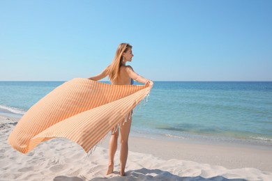Woman with beach towel near sea on sunny day, back view