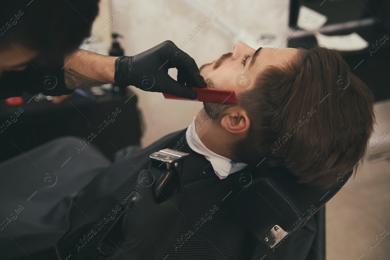 Photo of Hairdresser trimming client's beard in barbershop. Professional shaving service