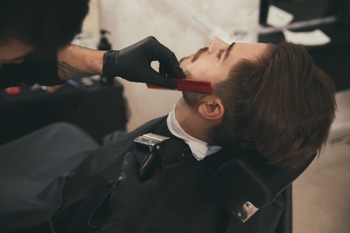 Photo of Hairdresser trimming client's beard in barbershop. Professional shaving service