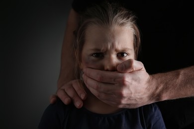 Photo of Man covering scared little girl's mouth on black background. Domestic violence