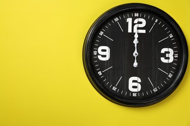 Photo of Modern black clock on yellow background, top view. Space for text