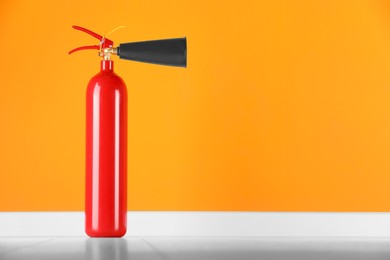 Fire extinguisher near orange wall, space for text