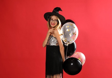 Beautiful woman in witch costume with balloons on red background. Halloween party