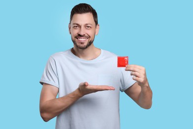Photo of Happy man holding condom on light blue background