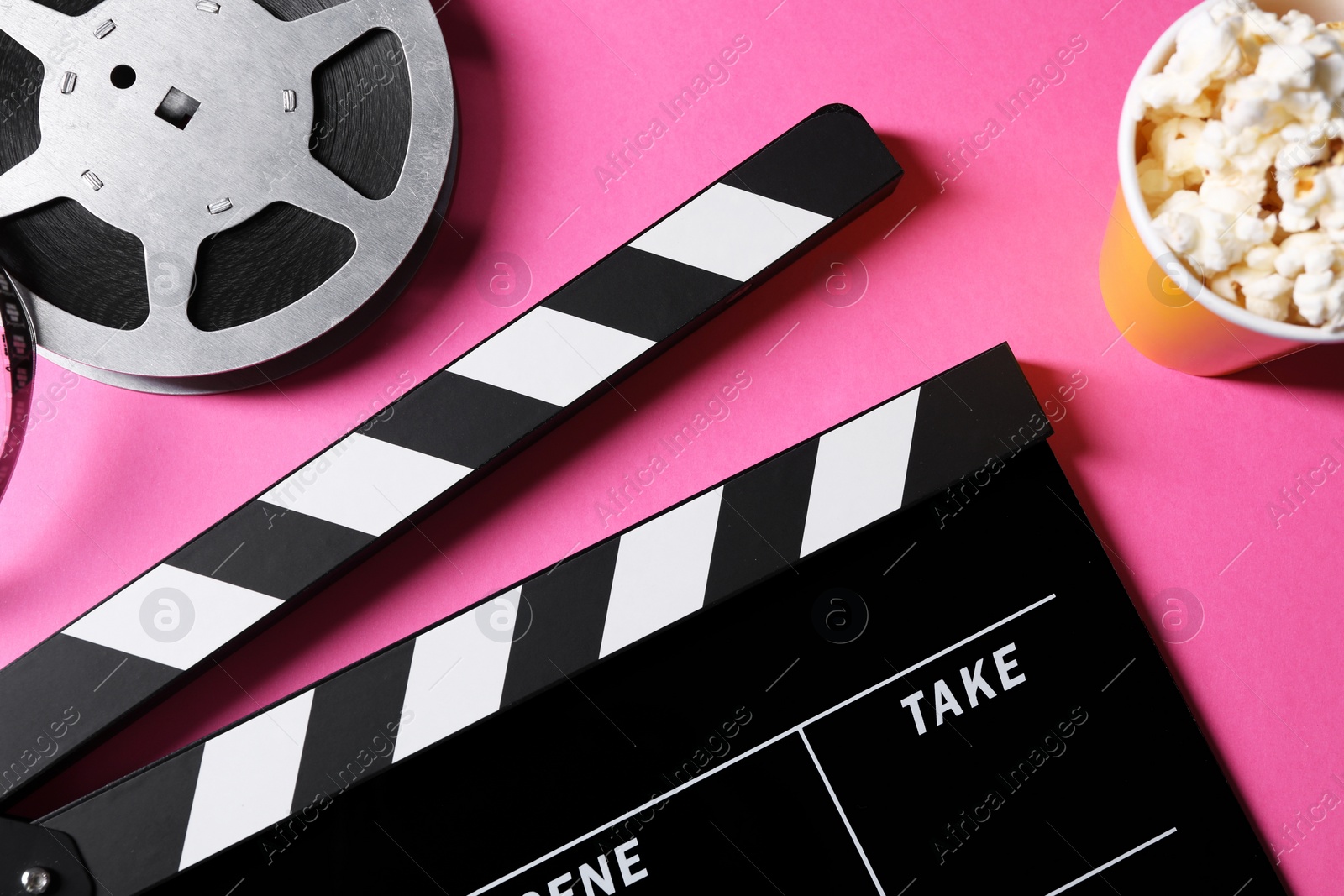 Photo of Clapperboard, popcorn and film reel on pink background, flat lay