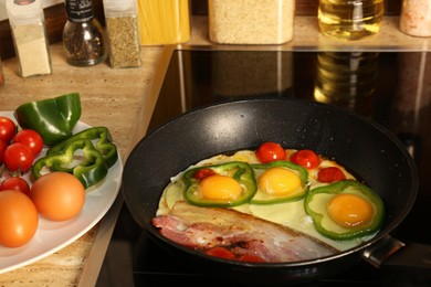 Cooking eggs with bacon, tomatoes and pepper in frying pan