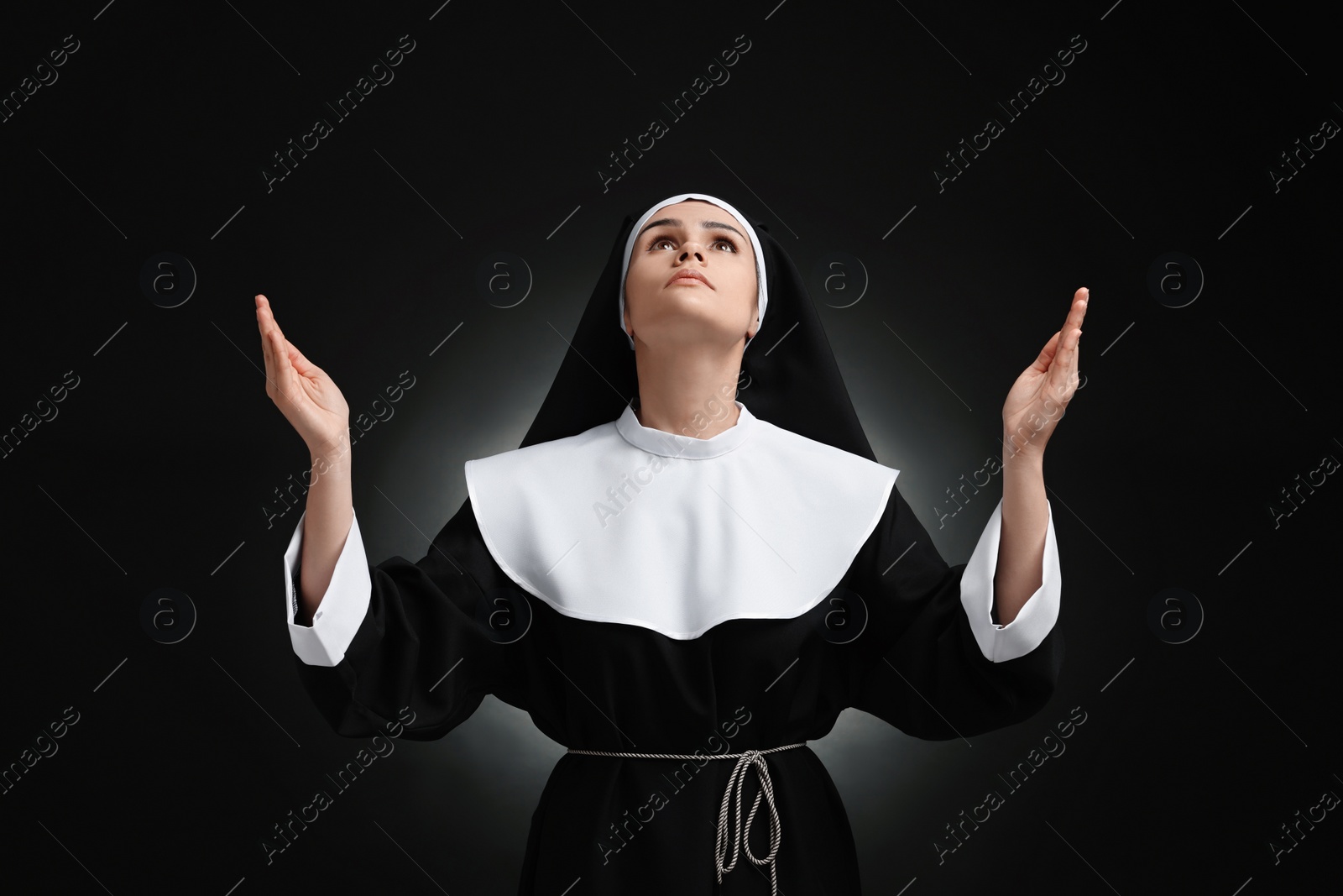 Photo of Nun praying to God on black background
