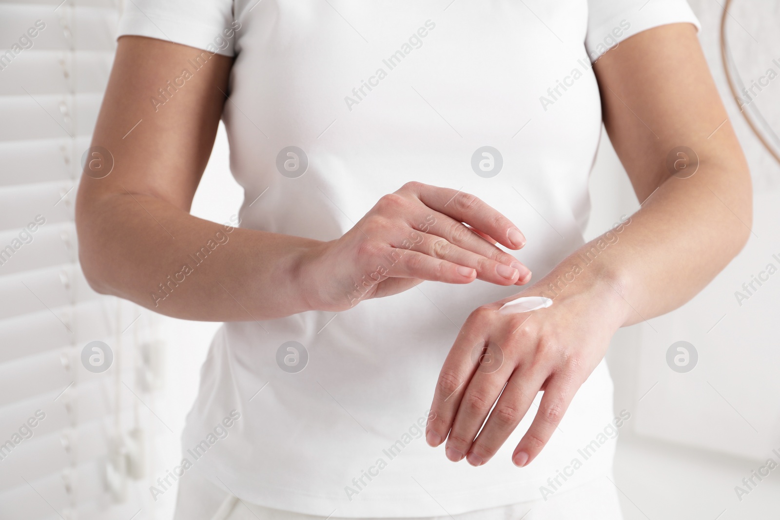 Photo of Woman applying cosmetic cream onto hand on blurred background, closeup