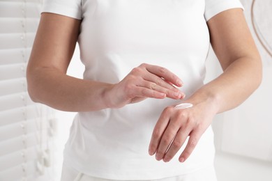 Woman applying cosmetic cream onto hand on blurred background, closeup