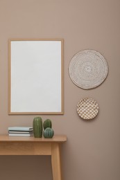 Photo of Empty frame hanging on beige wall over wooden table with decor. Mockup for design