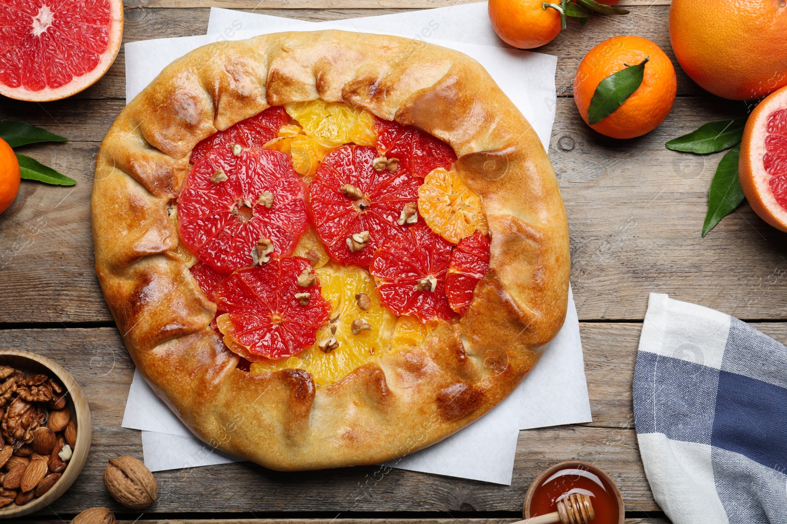 Photo of Delicious galette with citrus fruits and walnuts on wooden table, flat lay