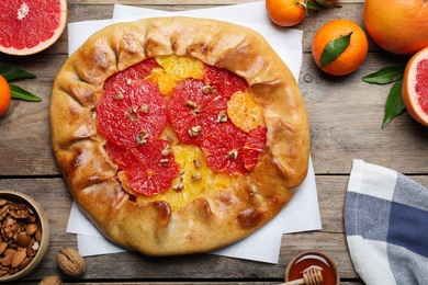 Delicious galette with citrus fruits and walnuts on wooden table, flat lay