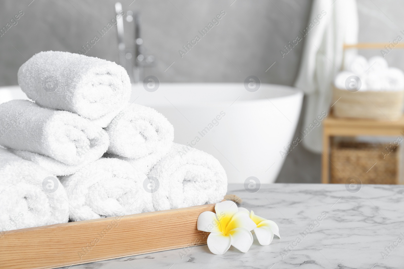 Photo of Rolled bath towels and beautiful flowers on white marble table in bathroom, space for text