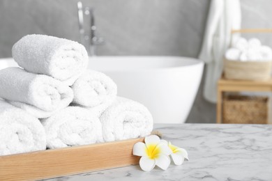 Photo of Rolled bath towels and beautiful flowers on white marble table in bathroom, space for text