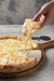 Photo of Woman taking piece of delicious cheese pizza at light grey table, closeup