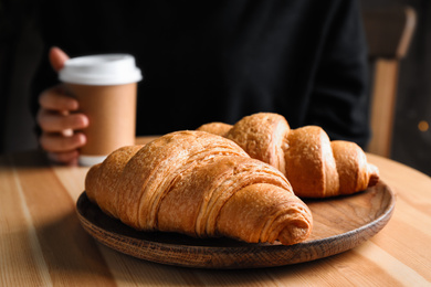 Photo of Tasty fresh croissants and woman with drink at wooden table, closeup