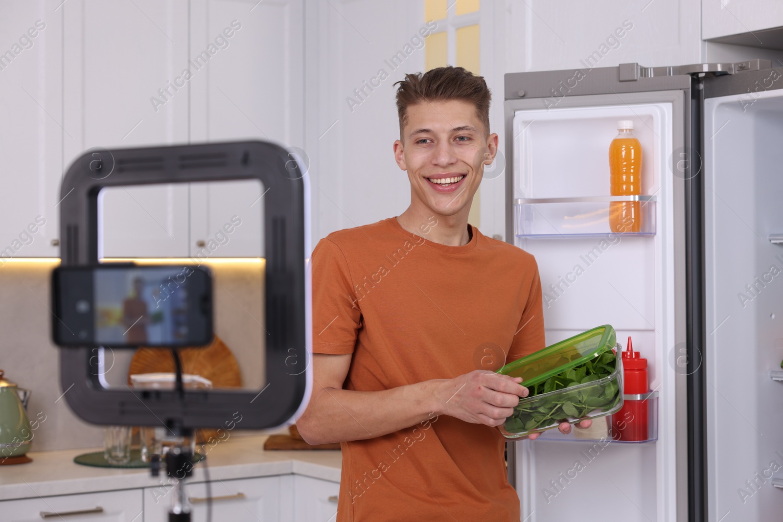 Photo of Smiling food blogger explaining something while recording video in kitchen