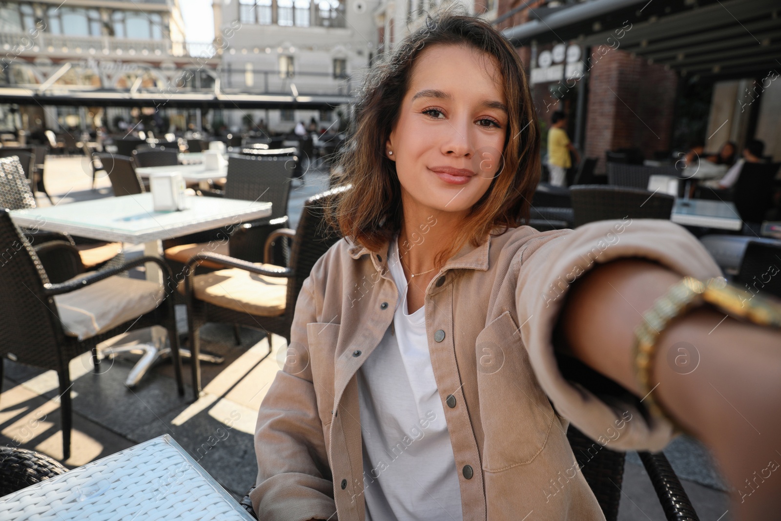 Photo of Happy young woman taking selfie in outdoor cafe