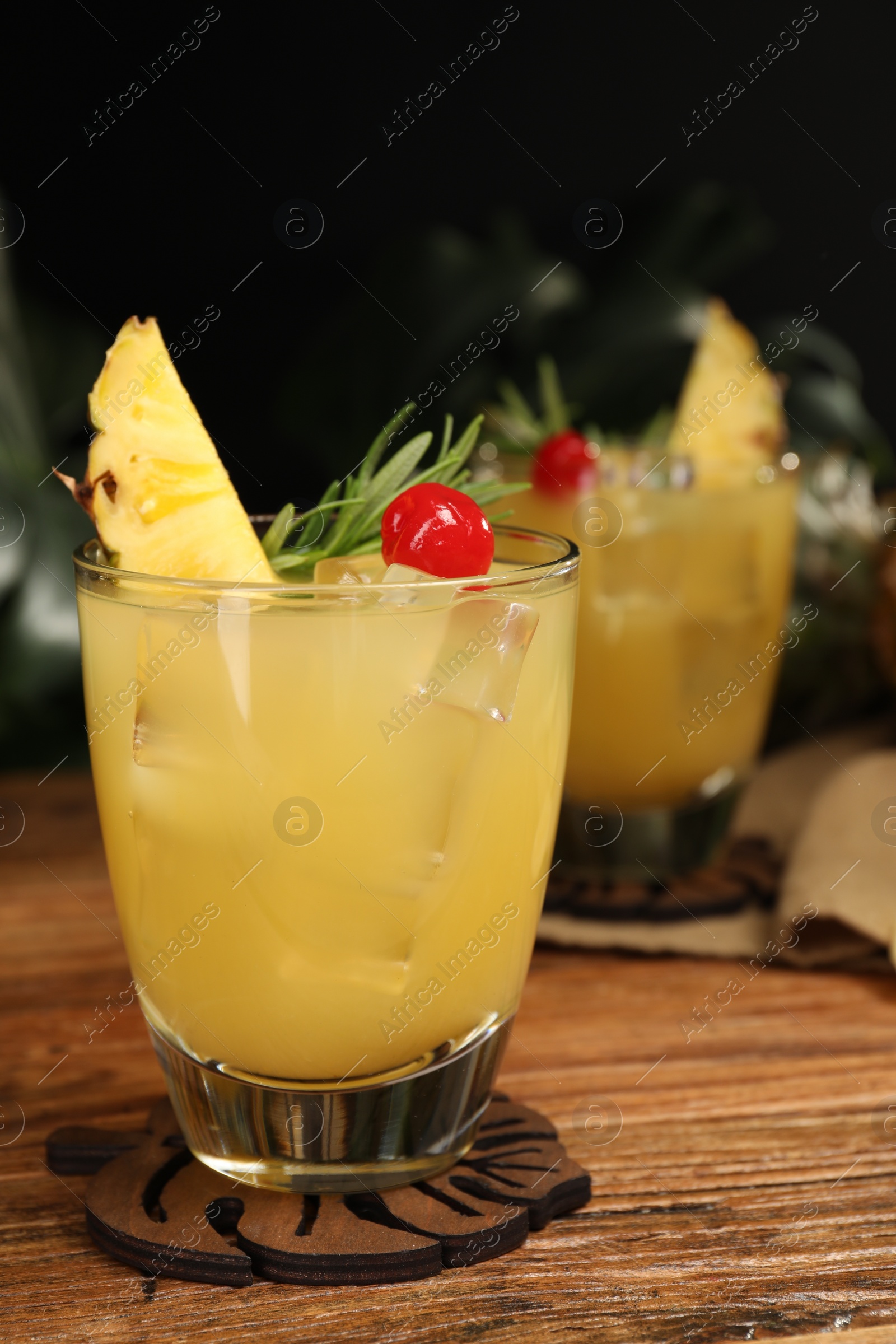 Photo of Glass of tasty pineapple cocktail with rosemary and cherry on wooden table