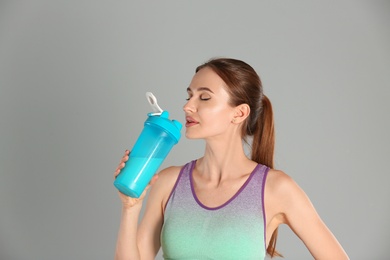 Athletic young woman drinking protein shake on light grey background
