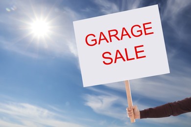 Man holding sign with text GARAGE SALE against blue sky