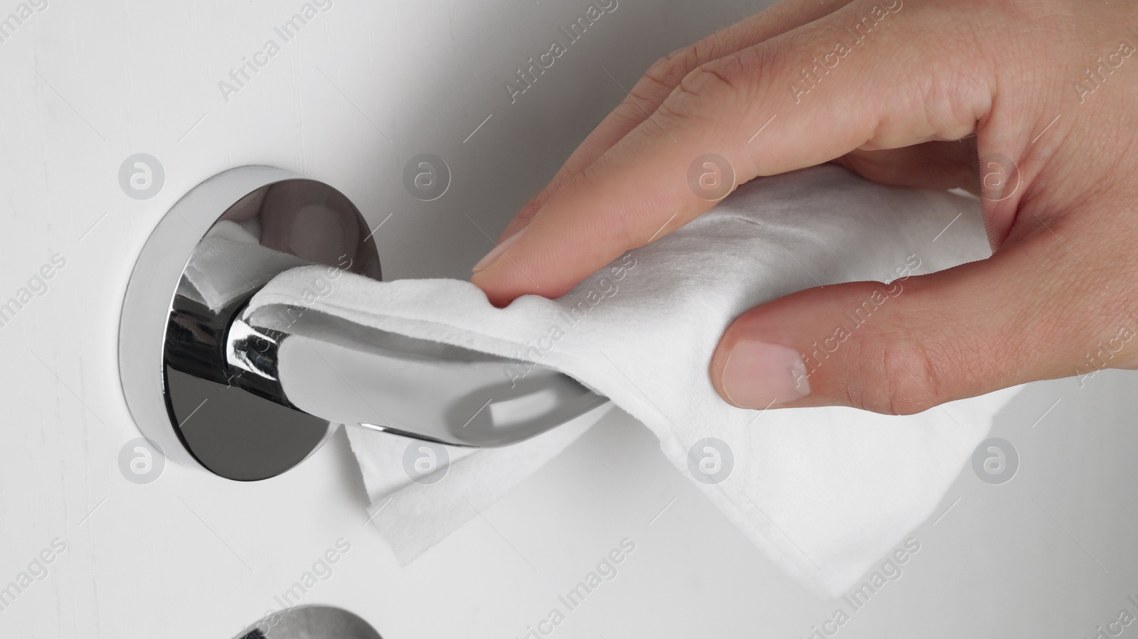 Photo of Man cleaning doorknob with disinfecting wipe indoors, closeup. Protective measures