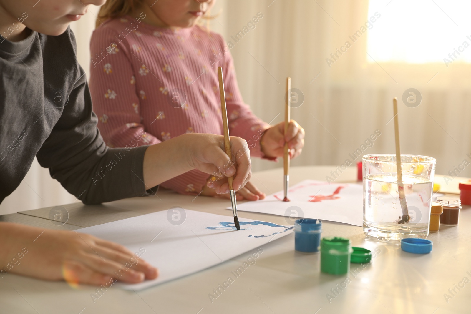 Photo of Little children drawing with brushes at wooden table indoors, closeup
