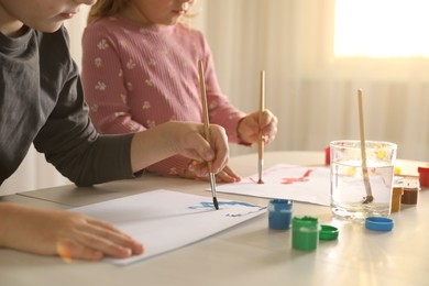 Little children drawing with brushes at wooden table indoors, closeup