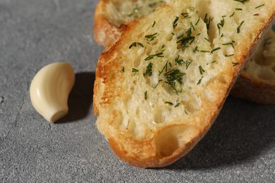 Tasty baguette with garlic and dill on grey textured table, closeup