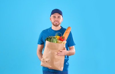 Photo of Delivery man holding paper bag with food products on color background