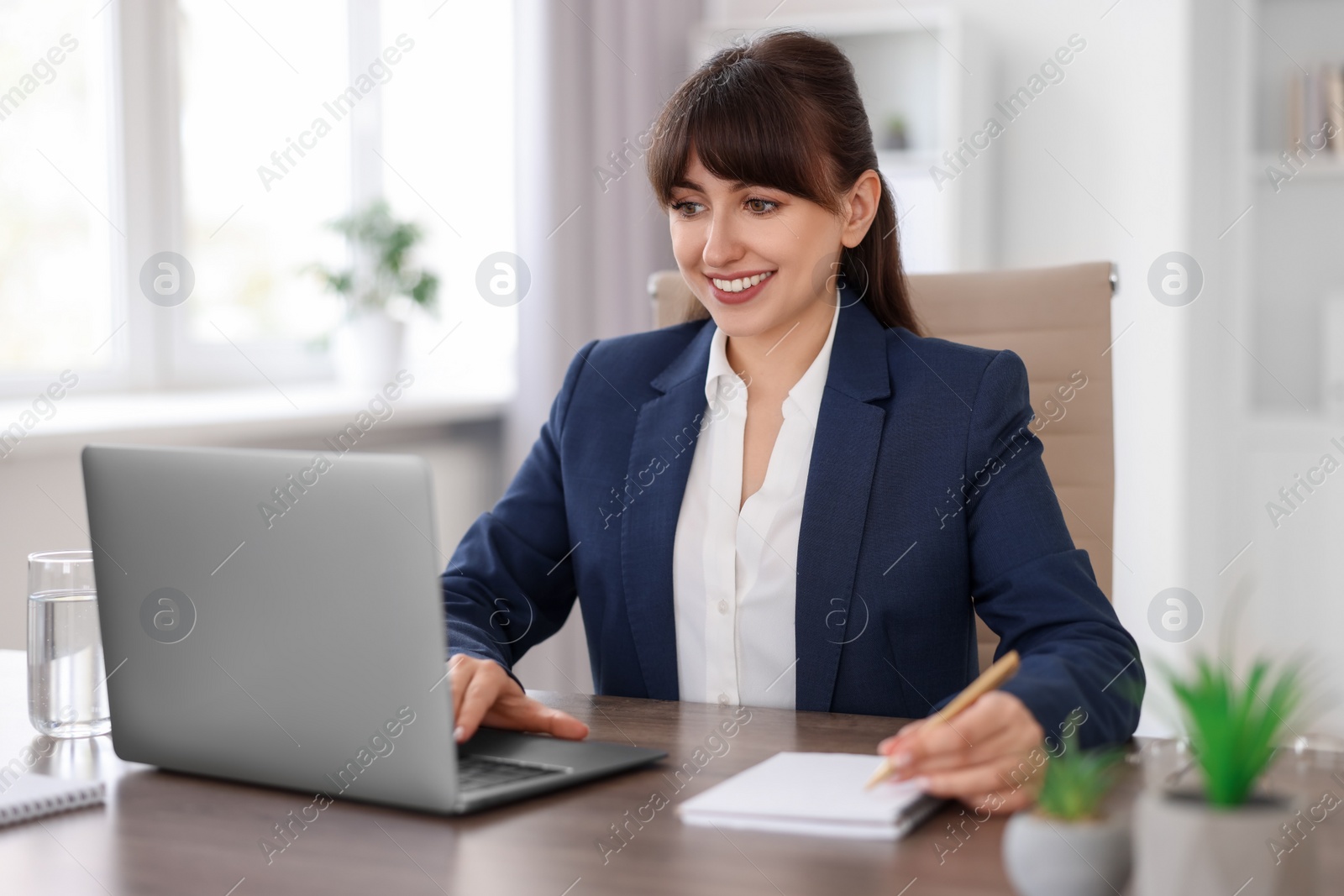 Photo of Woman taking notes during webinar at wooden table indoors