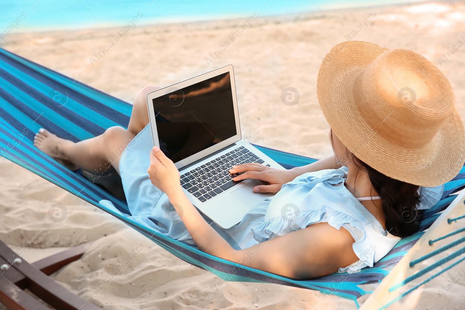 Photo of Young woman with laptop resting in hammock at seaside