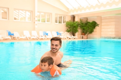 Photo of Father teaching son to swim with inflatable sleeves in indoor pool