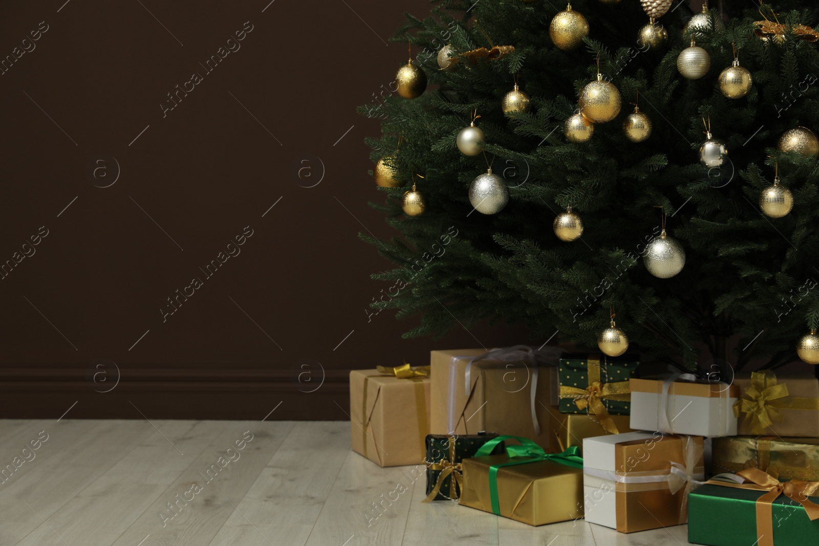 Photo of Beautifully decorated Christmas tree and many gift boxes near brown wall indoors, space for text