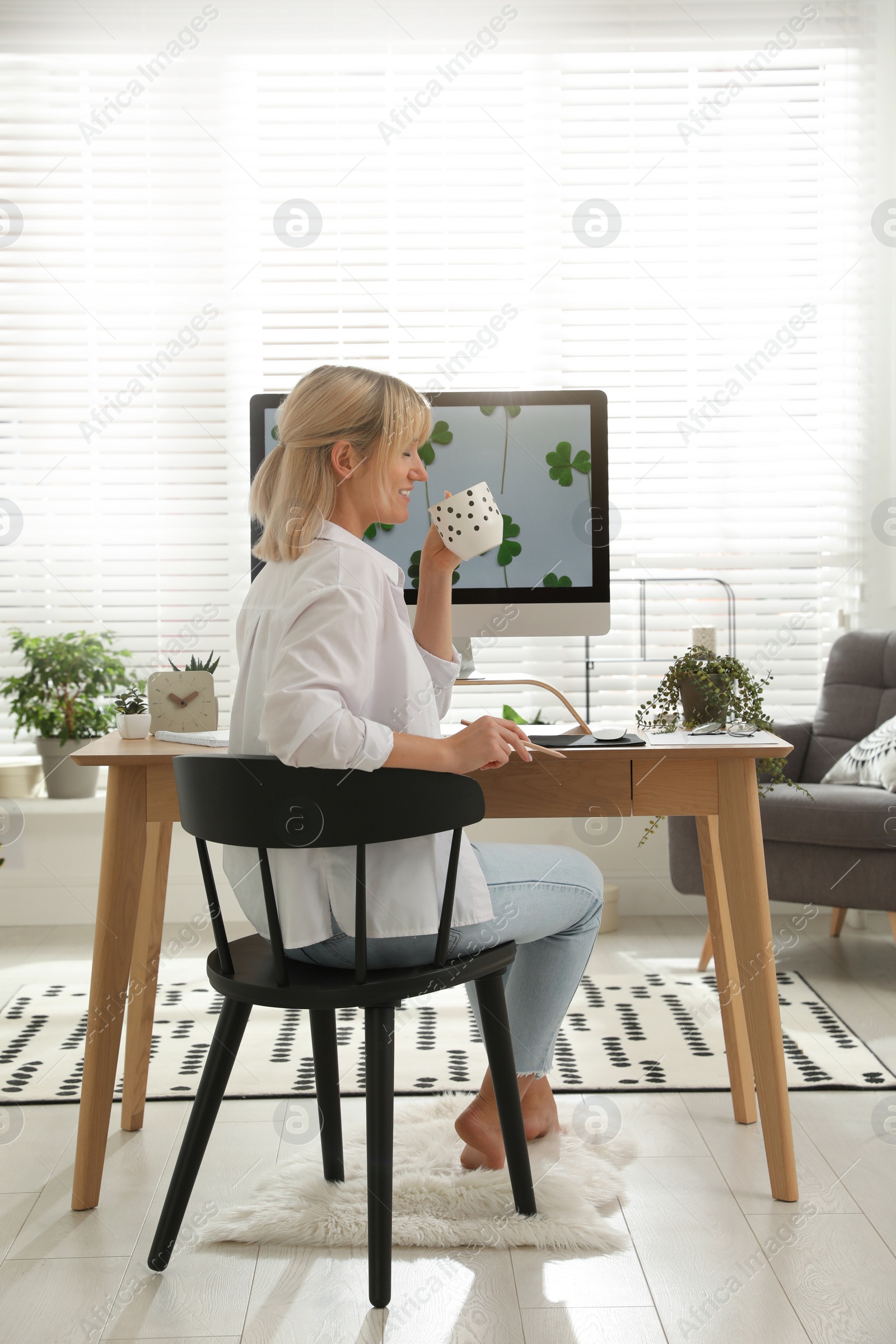 Photo of Woman with cup of tea at table in light room. Home office