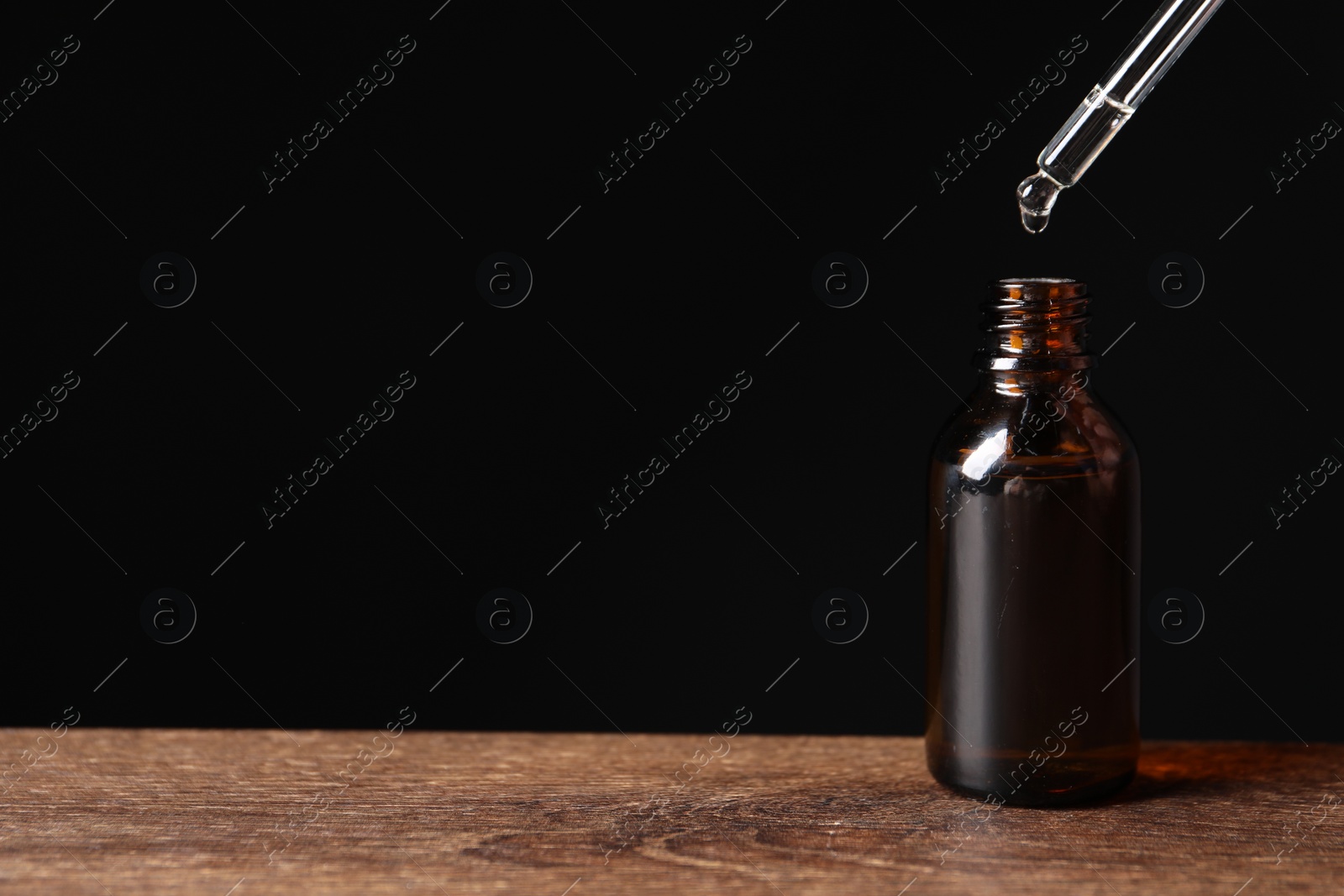 Photo of Dripping cosmetic serum from pipette into bottle on wooden table, space for text