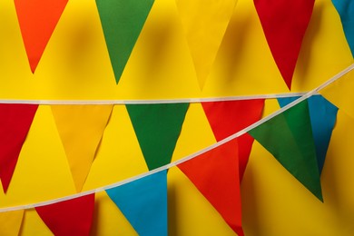 Photo of Buntings with colorful triangular flags hanging on yellow background. Festive decor