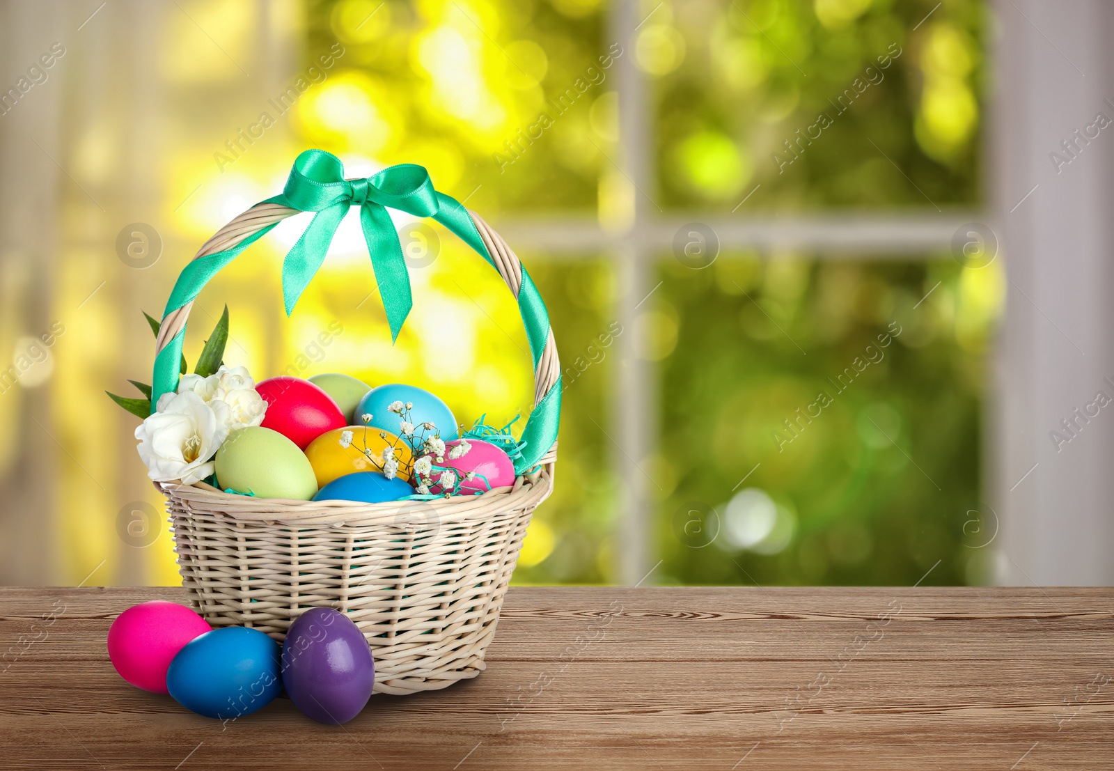 Image of Wicker basket with bright painted Easter eggs on wooden table, space for text