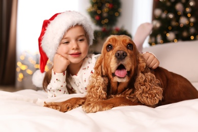 Cute little girl with English Cocker Spaniel on bed in room decorated for Christmas
