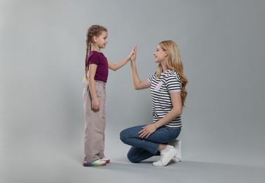 Mother and daughter giving high five on light grey background