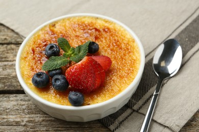 Photo of Delicious creme brulee with berries and mint in bowl on wooden table, closeup