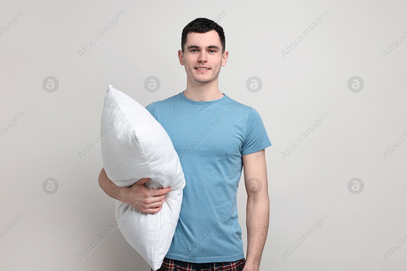 Photo of Happy man in pyjama holding pillow on light grey background