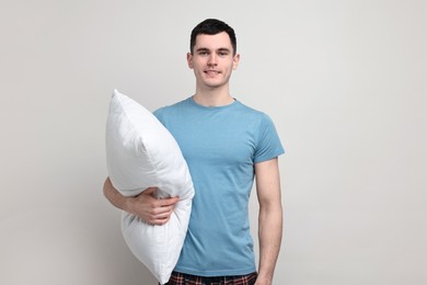 Happy man in pyjama holding pillow on light grey background